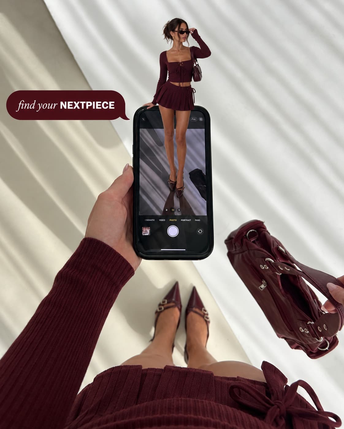 A creator in an oxblood knit set standing on a phone screen, with matching heels and shoulder bag below